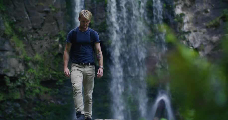 A man jumps on large stones by the waterfall