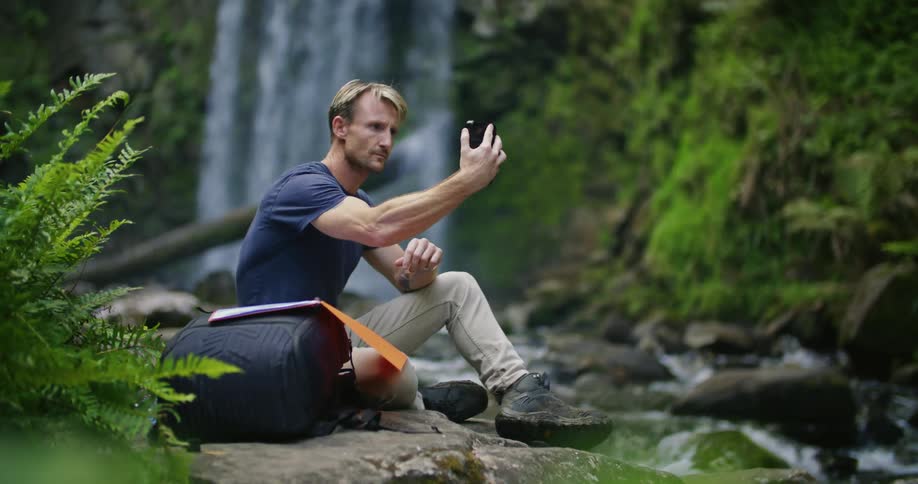 A man sitting next to a waterfall while hiking in nature