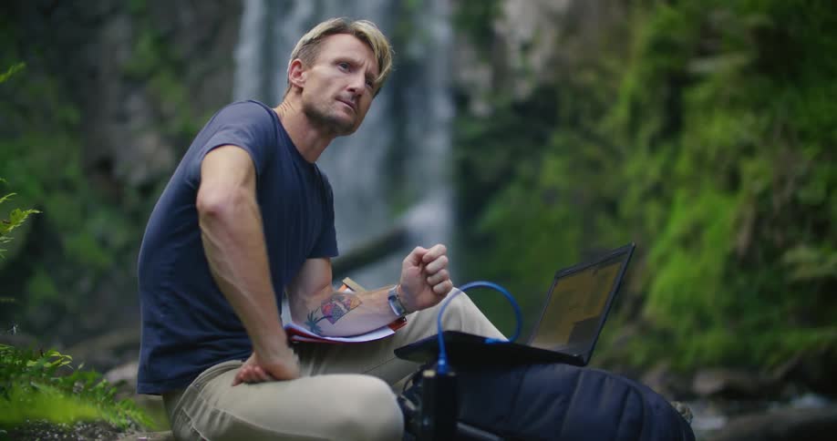 A man is typing on his laptop by the stream