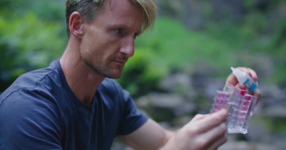 Man tests water sample while crouching next to water