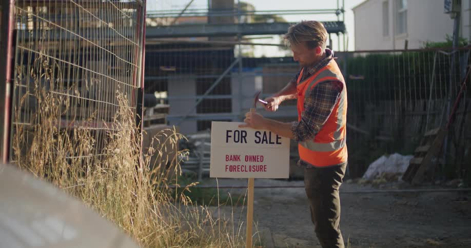 A construction worker hammering a for sale sign into the ground outside a property