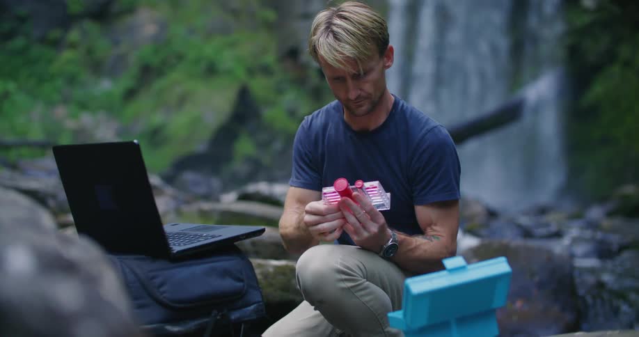 A man is collecting water samples by the stream