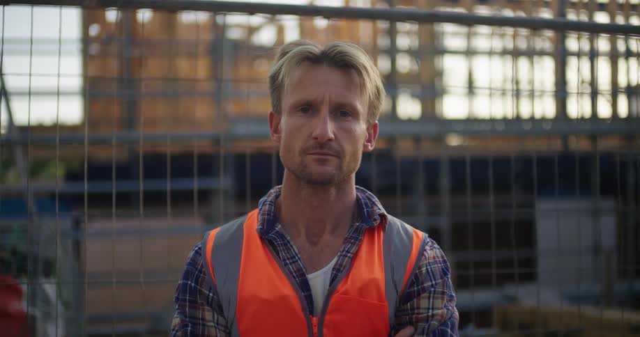 A male construction worker in an orange vest standing at a construction site