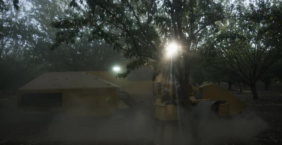A tractor is pulling a tree out of the ground in front of a cabana that is unfinished