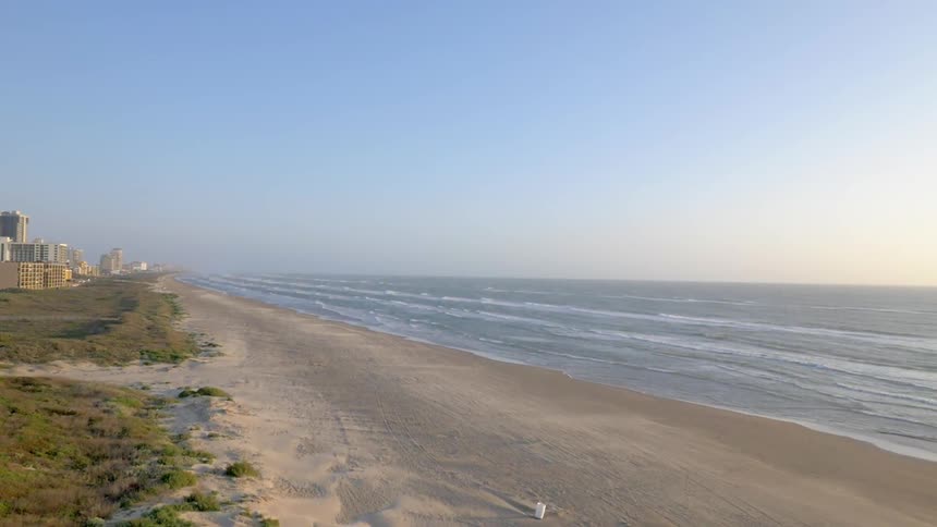 An empty beach stretches toward a group of high-rises in the distance