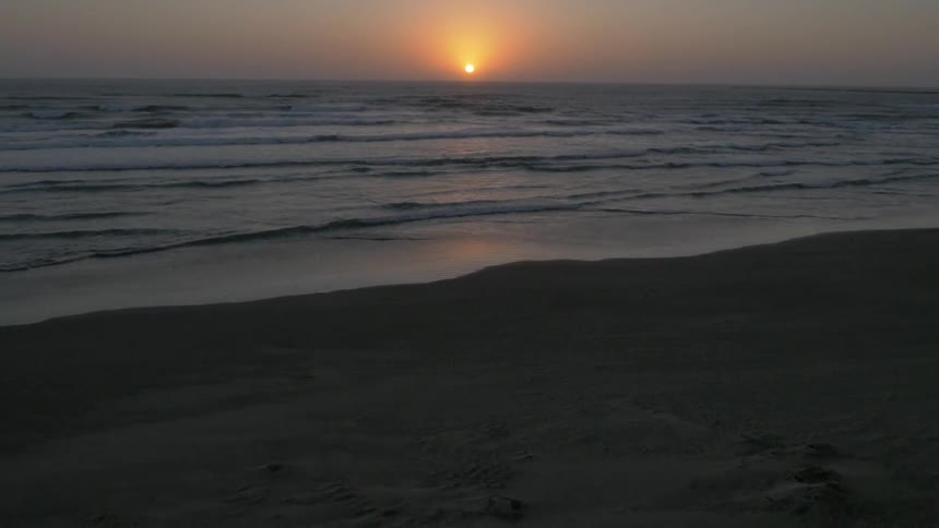 The waves crash against the shore at sunset