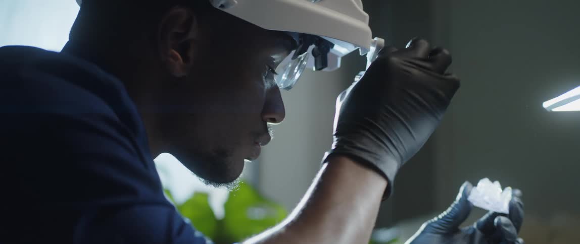 Man examines crystalline chunk using magnifying lens attached to headgear