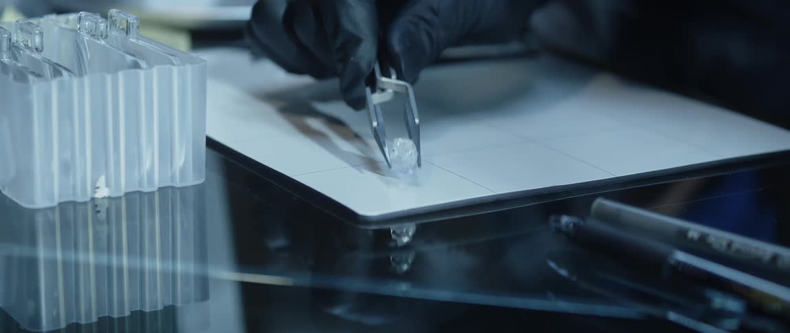 A diamond being placed on a white mat with tweezers