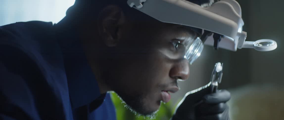 Man applies tool to gem after examining it through a magnifying glass