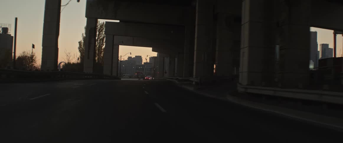Vehicle drives on highway under overpass at dusk