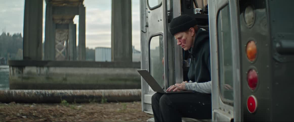 A woman types on a laptop while sitting in the open doors of a truck