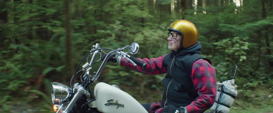 A woman rides a motorcycle on a road through a forest