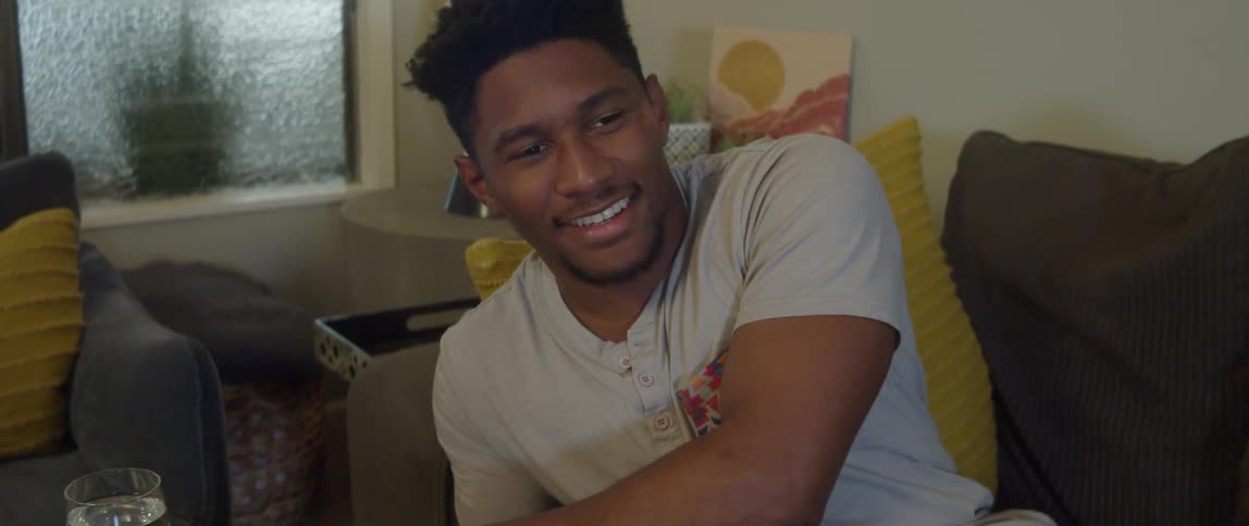 A man laughs while scrolling through his phone and watching TV