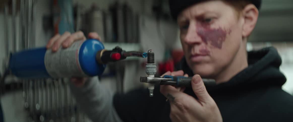 A woman uses a torch on a spark plug in her workshop