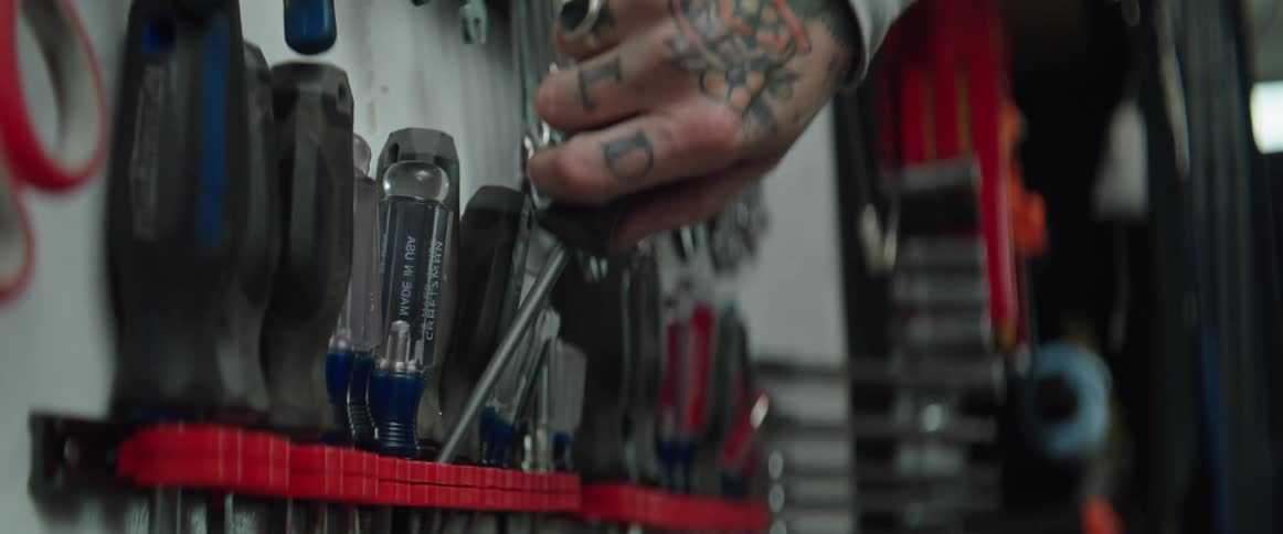 Close up of hand with tattoos ring and white shirt taking screwdriver at a garage