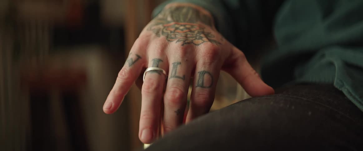 A person with hand tattoos tapping their fingers while sitting in a chair