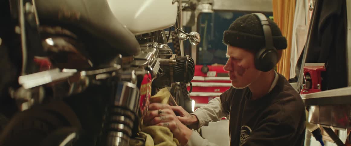 A person cleaning their motorcycle with a cloth in a garage while wearing headphones and listening to music