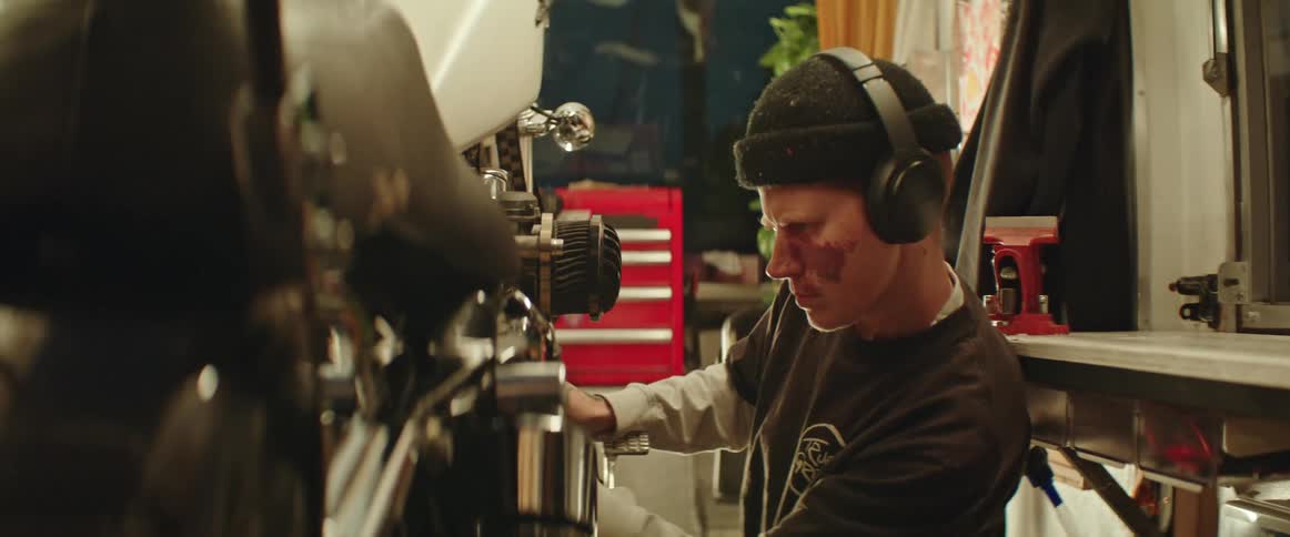 A person wearing a black hat and headphones cleaning a motorcycle