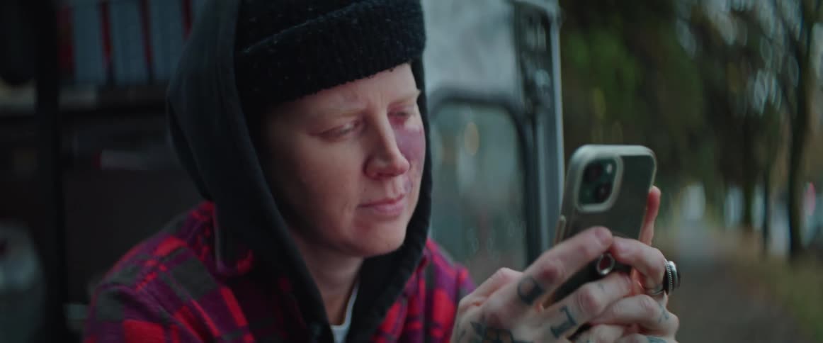 A woman is wearing a hat sitting outside looking at her phone
