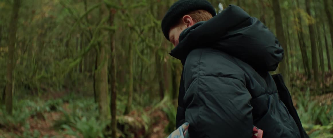 Woman with black hat and coat walks in green forest