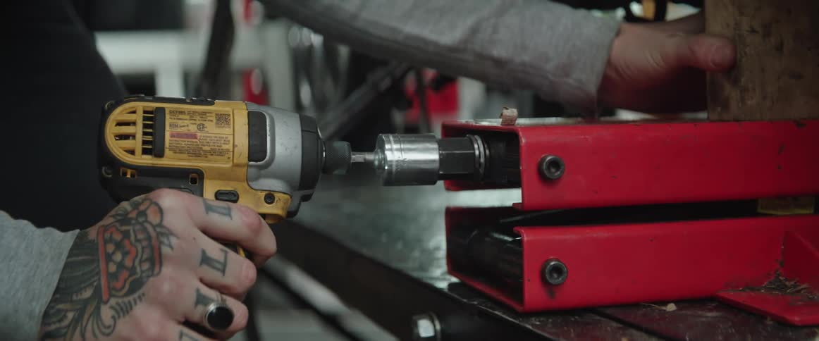 A woman with hand tattoos using a power drill in a workshop