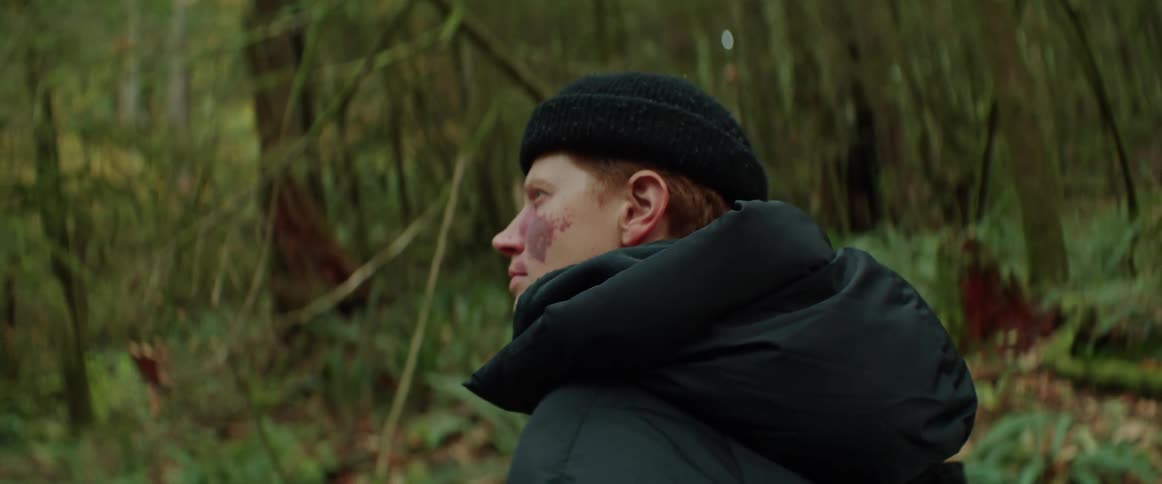 A close up of a person wearing a black coat and hat walking through the forest