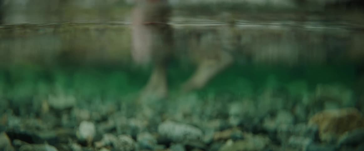 Semi-submerged view of a person's legs walking through clear water in a natural pool