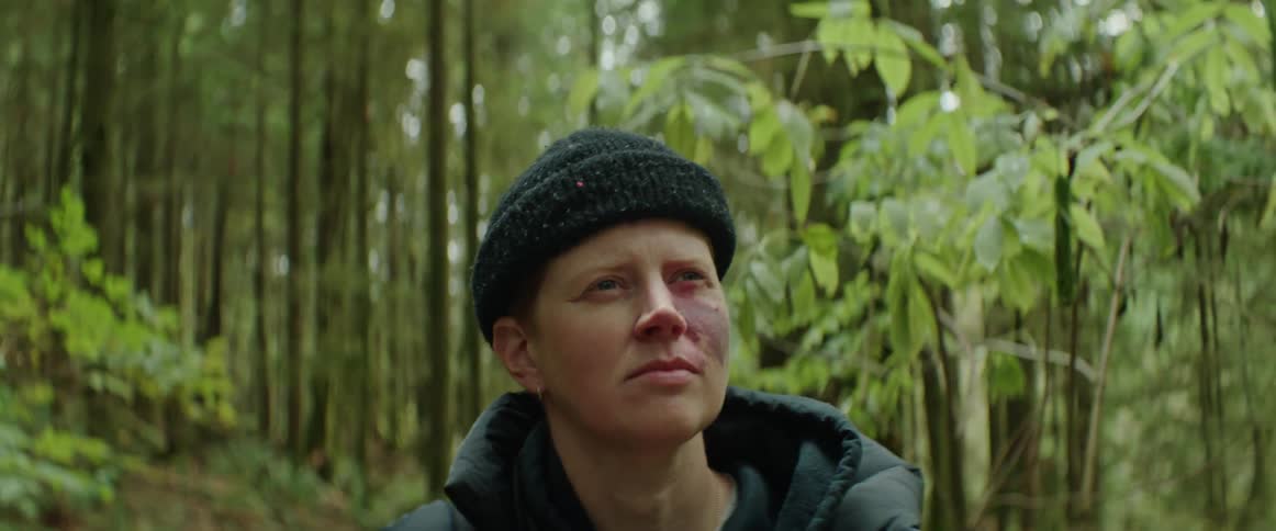 A woman wearing a black hat and coat walking through a forest