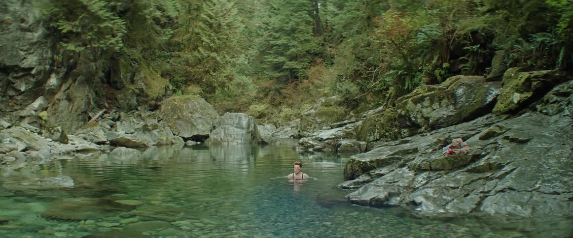 A woman submerges herself into a cold pool in a secluded forest location