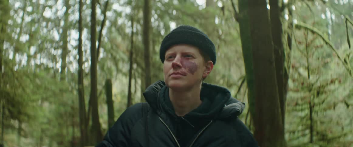 A person wearing a black hat and coat walking through a forest