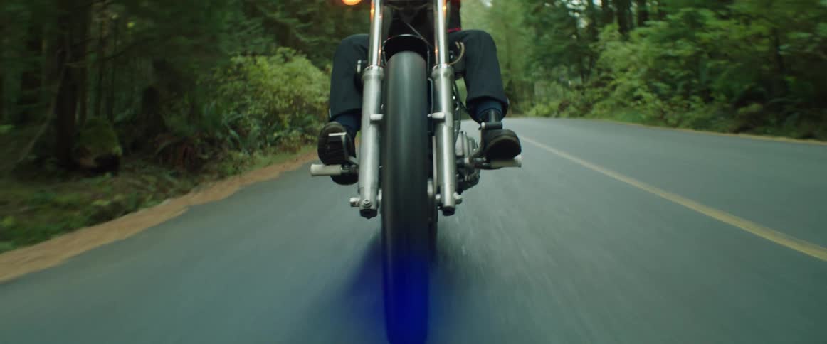 A person riding a motorcycle on a paved road lined with trees and vegetation