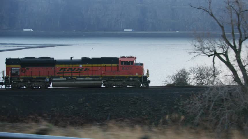 Reveal of a freight train shows scene with semi trucks and another freight train in the background along the Columbia River in the Pacific Northwest