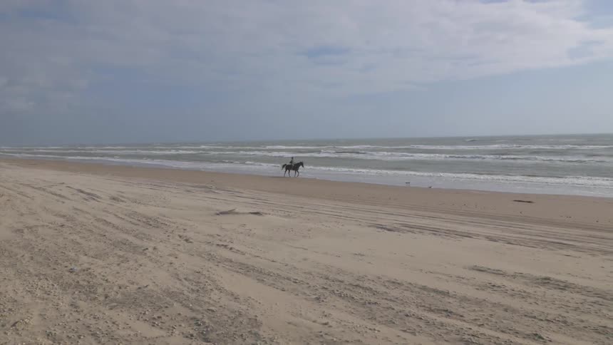 Someone riding a horse along the beach on a cloudy day