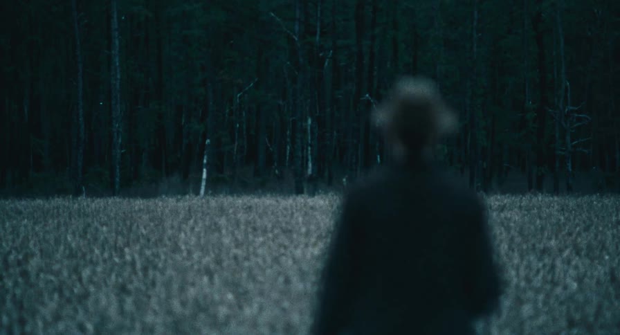A man walks through a snowy field toward the forest