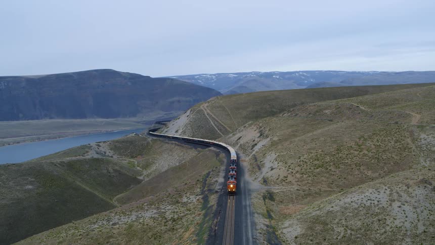 A long freight train slowly winds its way through rugged foothills
