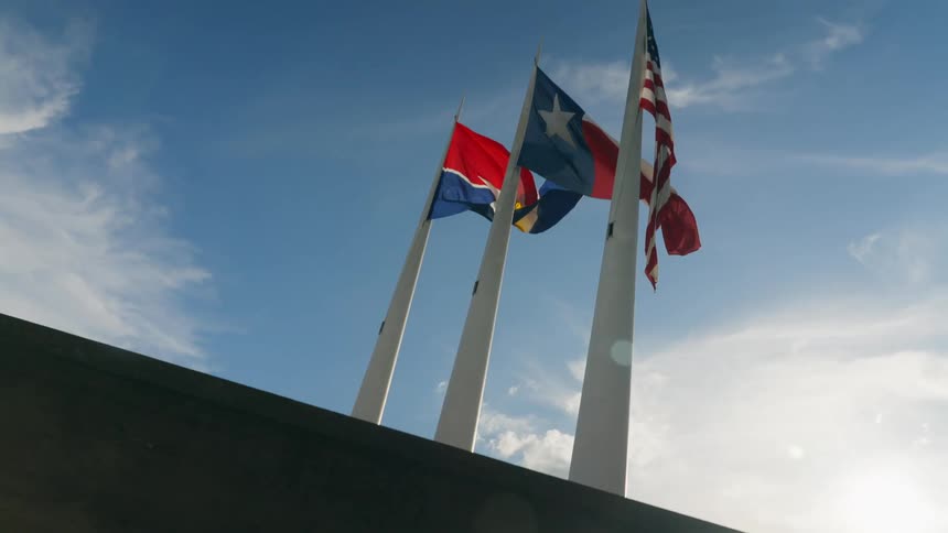 The sun shines down on three raised flags
