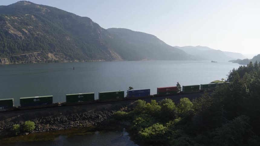 A double stack container train travels through a beautiful river gorge