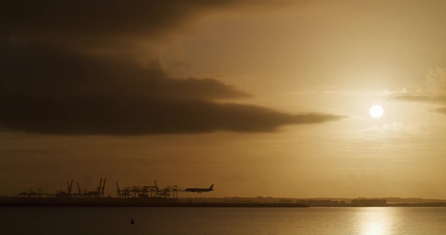 Distant passenger plane coming down through the air onto the ground at sunset