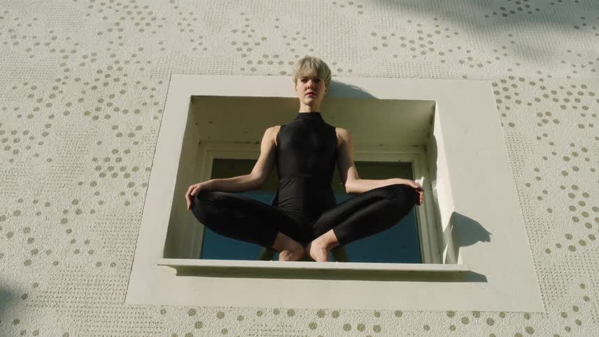 A sad looking woman perched on a window ledge high up off the ground