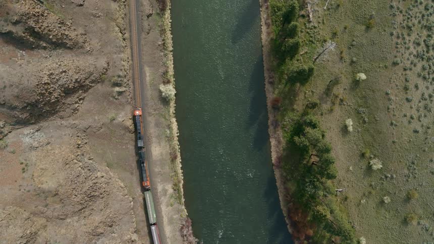 Birds eye view following the lead locomotives of a freight train pulling cargo in a steep river gorge