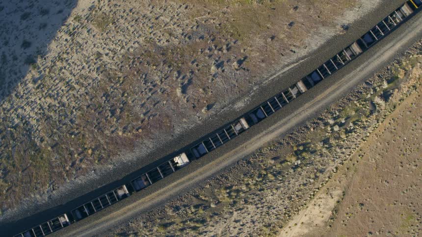 Descending twist over empty hopper cars moving on curved track between sandy dunes