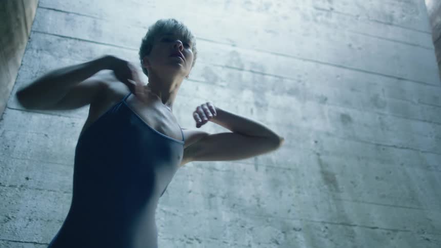 A dancer performs a modern style dance in front of a cement wall