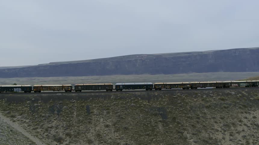 Slow push towards freight cars traveling past cliffs and steep hills in the countryside