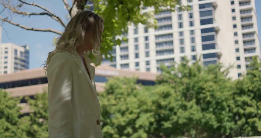 A woman holding a camera is walking her dog through a city park