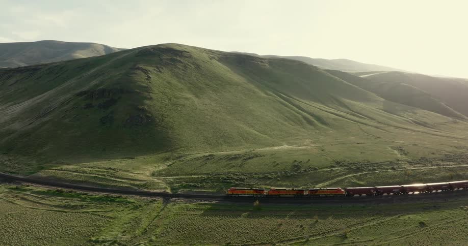 A freight train makes its way through beautifully lit rolling hills