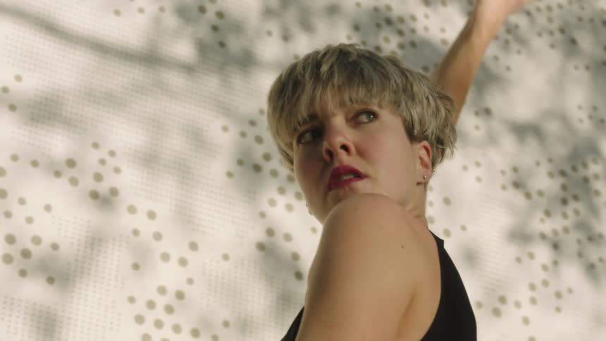 A woman with short blond hair is dancing and moving her shoulders and arms as she turns her head