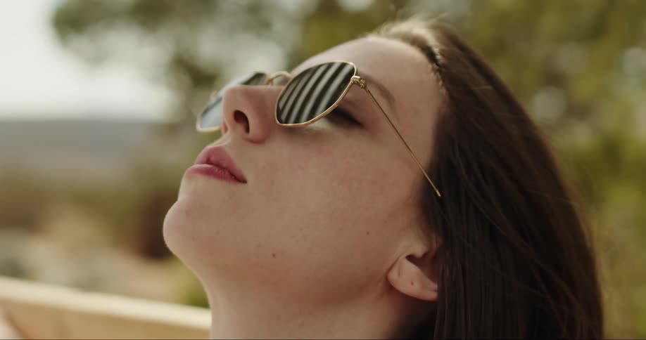 A woman in sunglasses sits outside with her head tilted up
