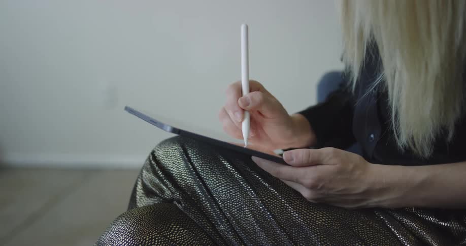 A woman sitting with legs crossed using a stylus to draw and sketch on a tablet