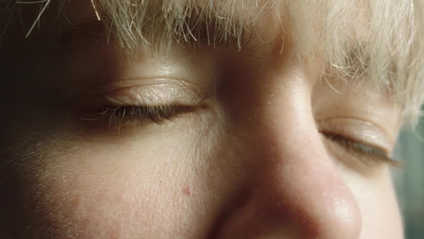 Blonde person with hazel eyes slowly closes and opens their eyes