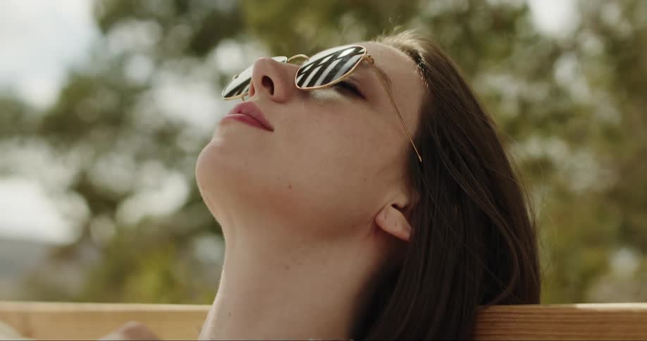 A young woman leaning her head back on a bench while the sun shines down on her
